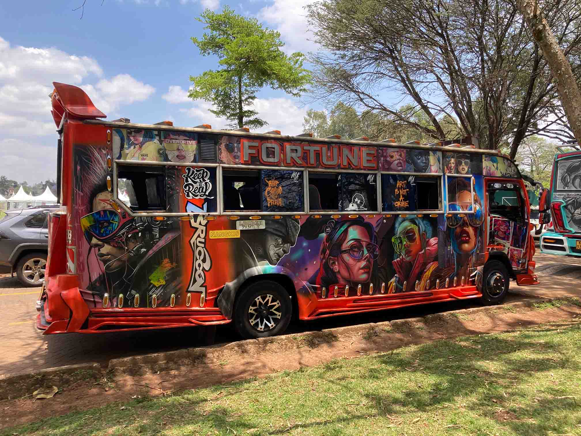 A vibrant and colorful Kenyan matatu (minibus) named “FORTUNE,” adorned with detailed graffiti art featuring futuristic and pop culture themes, parked in a shaded area.