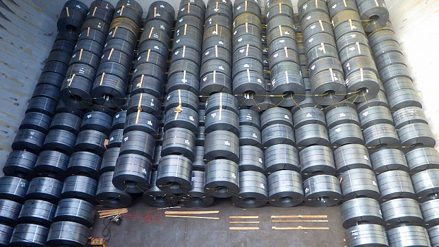 Numerous large metal coils are neatly stacked and secured in rows, illustrating the cargo load of steel products within a ship’s hold, ready for transport.