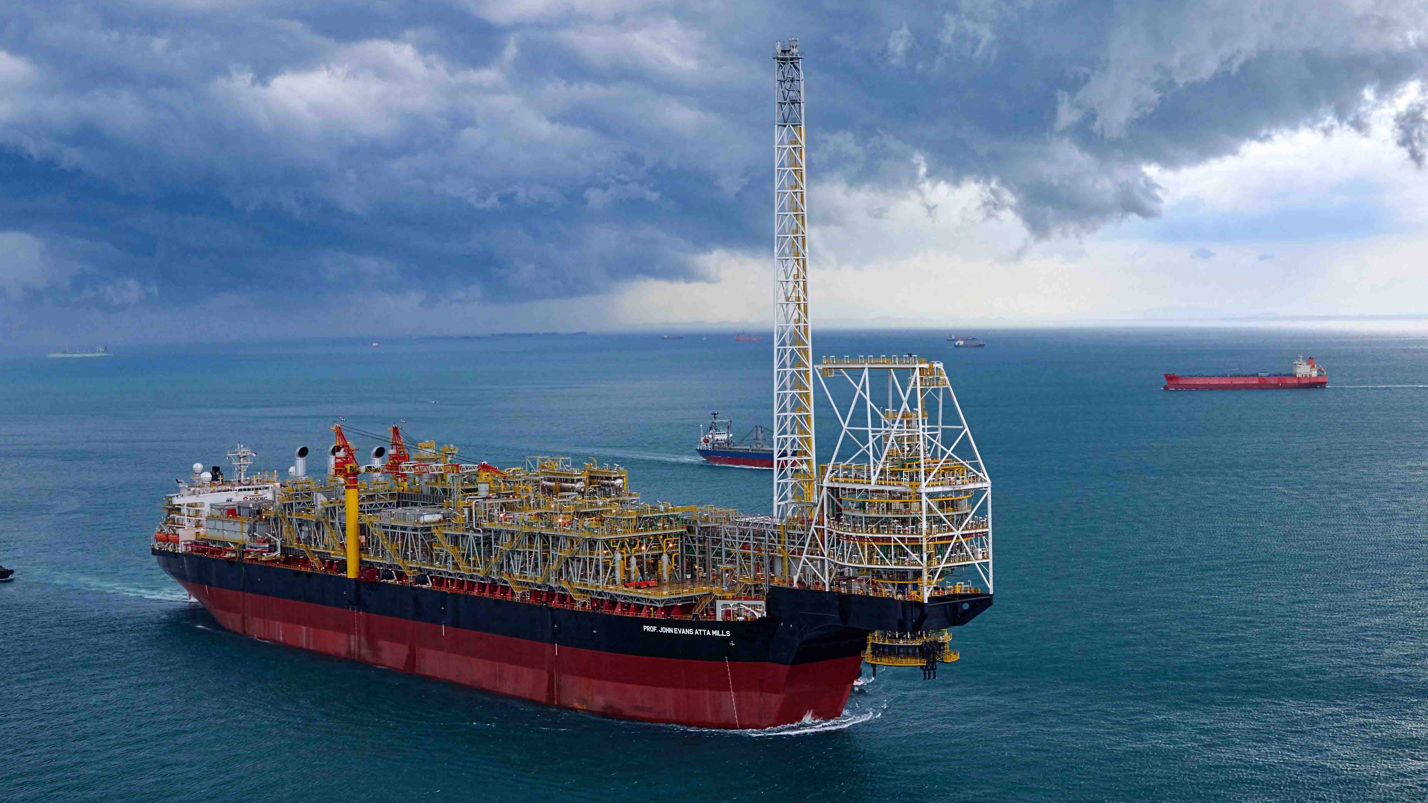 The offshore FPSO vessel ‘PROF. JOHN EVANS ATTA MILLS’ operates in calm waters, with its extensive infrastructure visible under a cloudy sky, showcasing offshore oil production and storage capabilities.