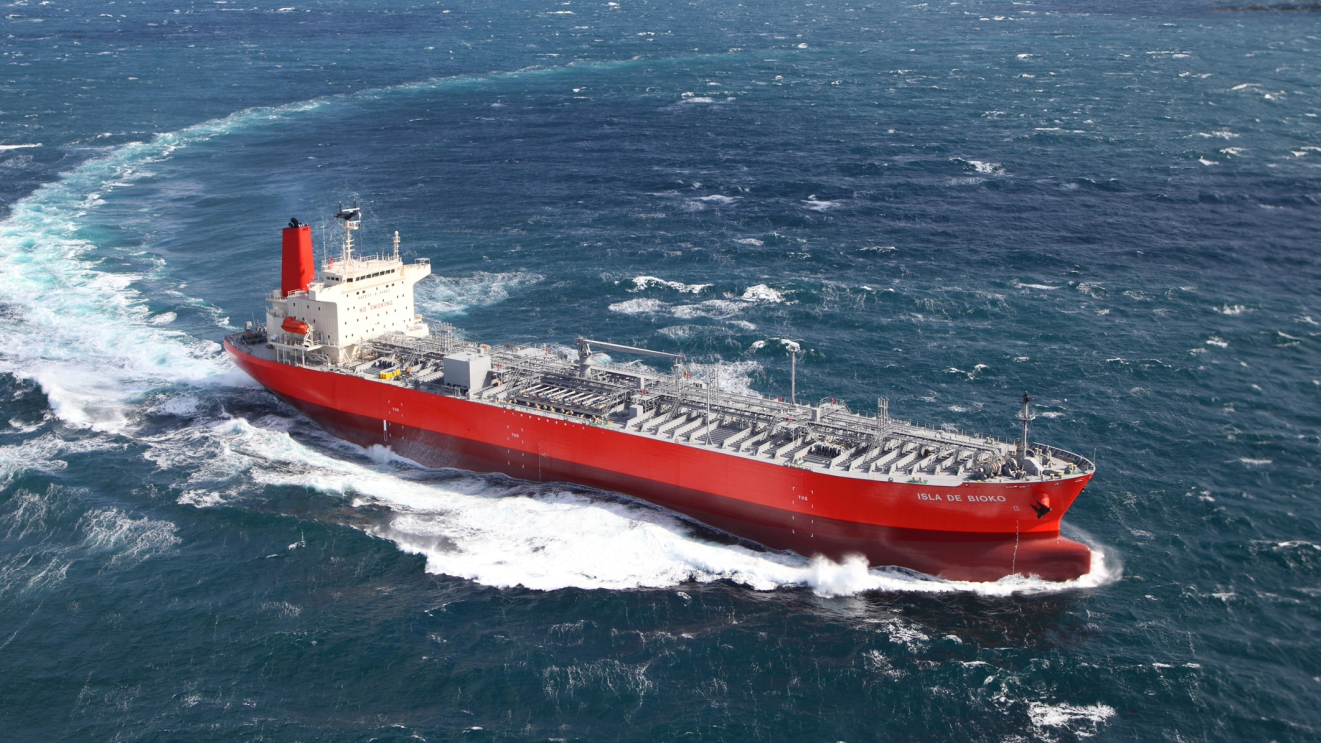 A large red tanker named ‘ISLA DE BIOKO’ sails through rough seas, cutting through the waves with its bow, showcasing the vessel’s robust capabilities.