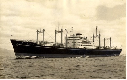 A black-and-white photograph of a vintage cargo ship Panamamaru with multiple masts and visible flags, cruising on the open sea.