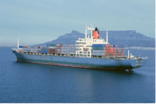 A large container ship Osakamaru loaded with colorful shipping containers, sailing in front of a mountainous backdrop under a clear sky.