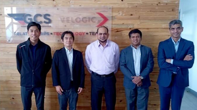 Five men stand together in front of a wooden wall with the GCS and VELOGIC logos, symbolizing a partnership between MOL and GCS Velogic in Africa.