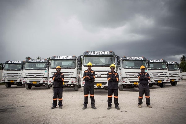 Four uniformed workers stand in front of a row of large Alistair trucks under a cloudy sky, showcasing the fleet and team readiness for operations.